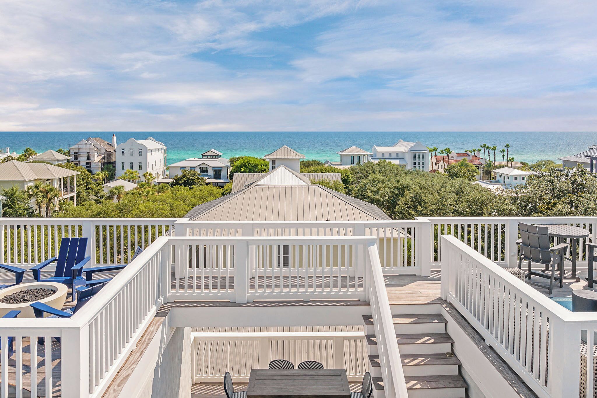 A deck with outdoor seating, a fire pit, and a view of the ocean and other buildings.