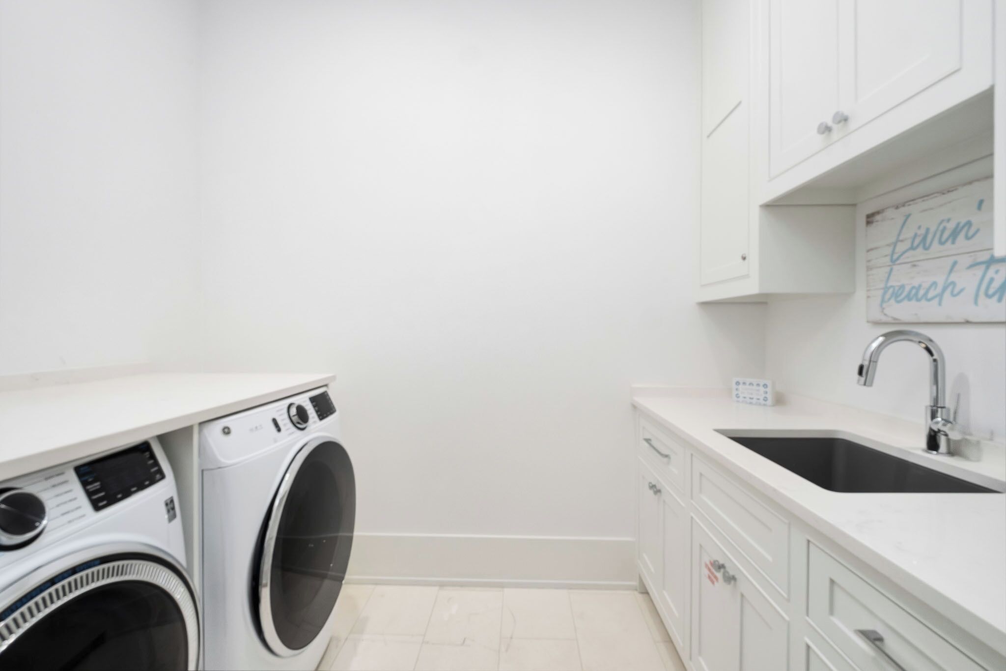 A laundry room with a washing machine, a sink, and a sign that says "livin' beach time".