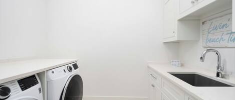 A laundry room with a washing machine, a sink, and a sign that says "livin' beach time".