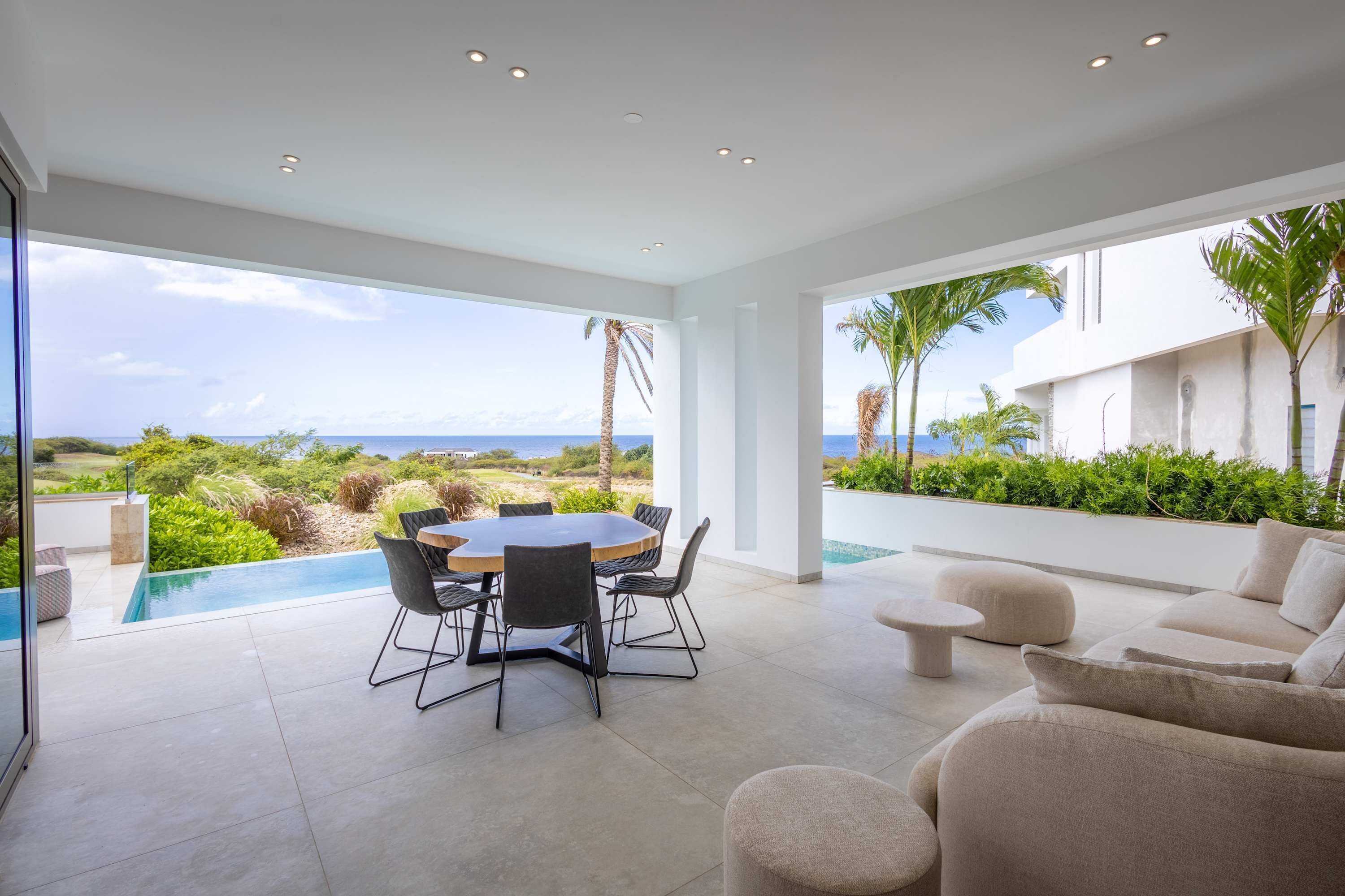 Un área de comedor exterior moderna con piscina, con vistas a un paisaje exuberante y el mar.