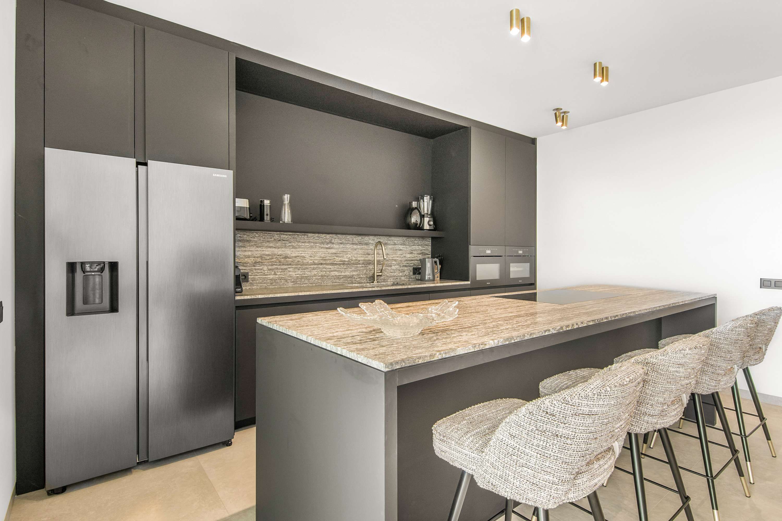 A modern kitchen with a large island, stainless steel appliances, and bar stools.