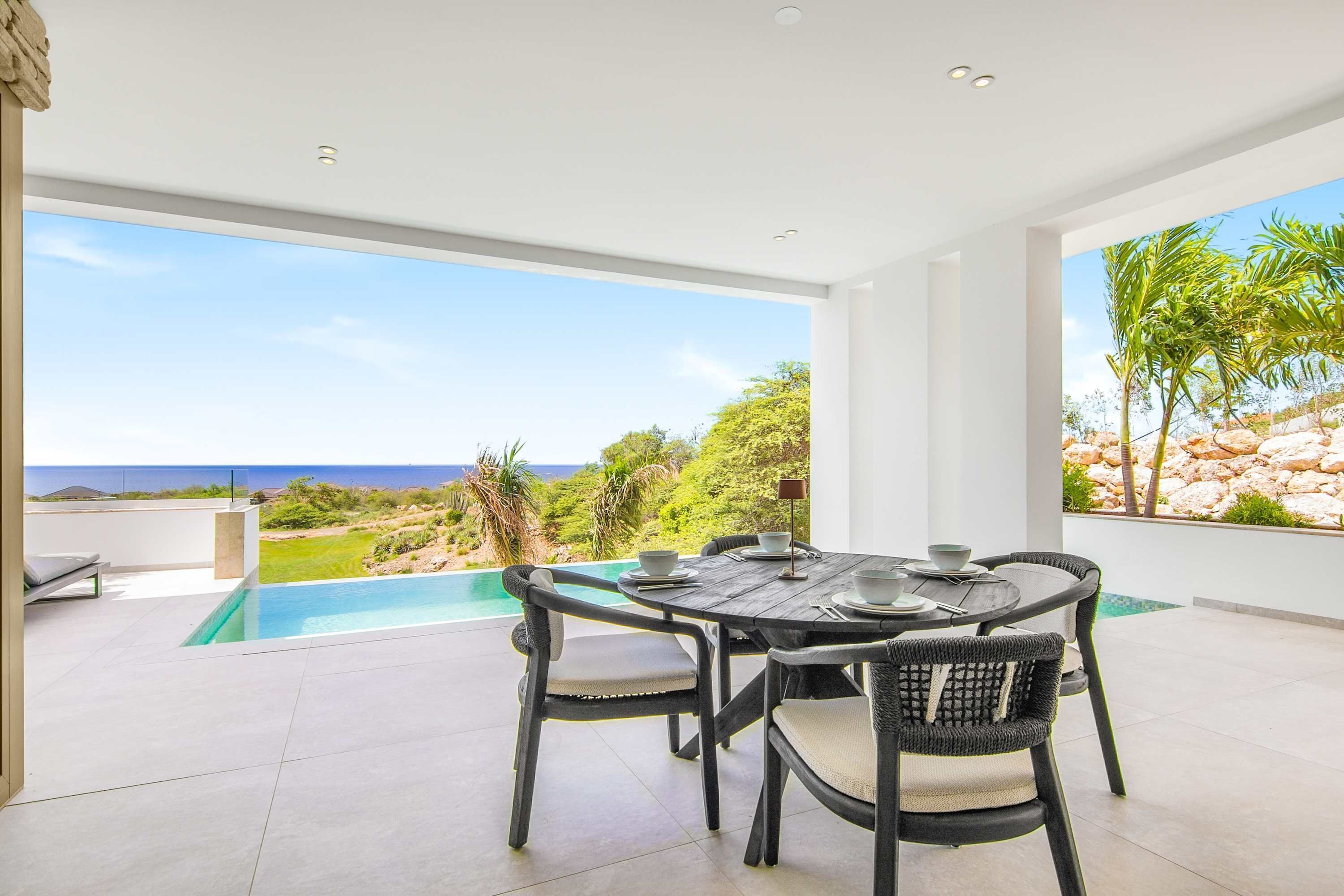 Uma zona de refeições com vista para o oceano, piscina e jardim.