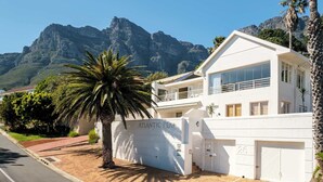 A modern building with a prominent entrance labeled "ATLANTIC PEARL," featuring a large palm tree in the foreground, a mountain backdrop, and a clear sky. - Classic Charm Meets Modern Comfort at Atlantic Pearl (Cape Town)