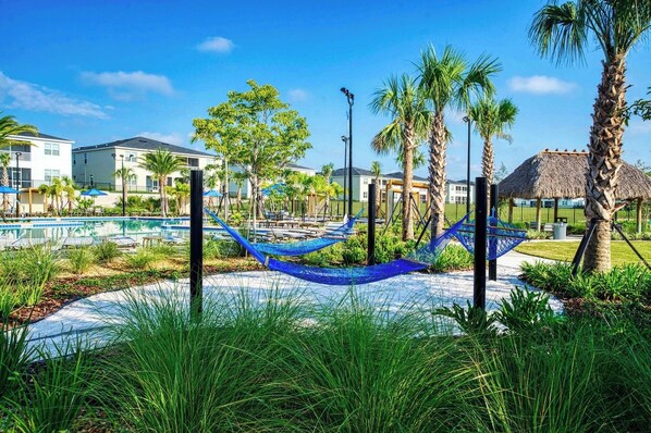 Ein Resort mit Swimmingpool, Hängematten, Palmen und einem Gebäude mit Reetdach.