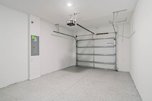 Una habitación limpia y vacía con una puerta blanca, un proyector instalado en el techo y una estantería de metal.