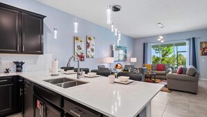 A modern kitchen with a large island, dark cabinetry, and pendant lighting.