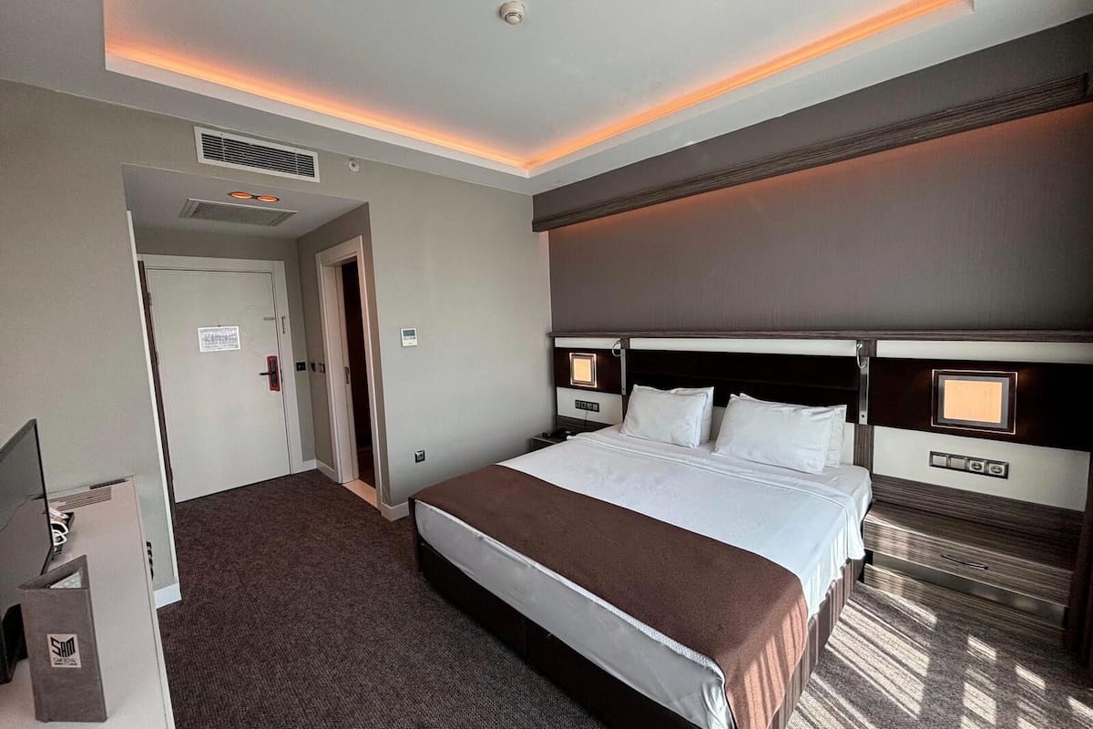 A hotel room with a large bed, a flat-screen TV, a desk, and a bathroom visible through an open door.