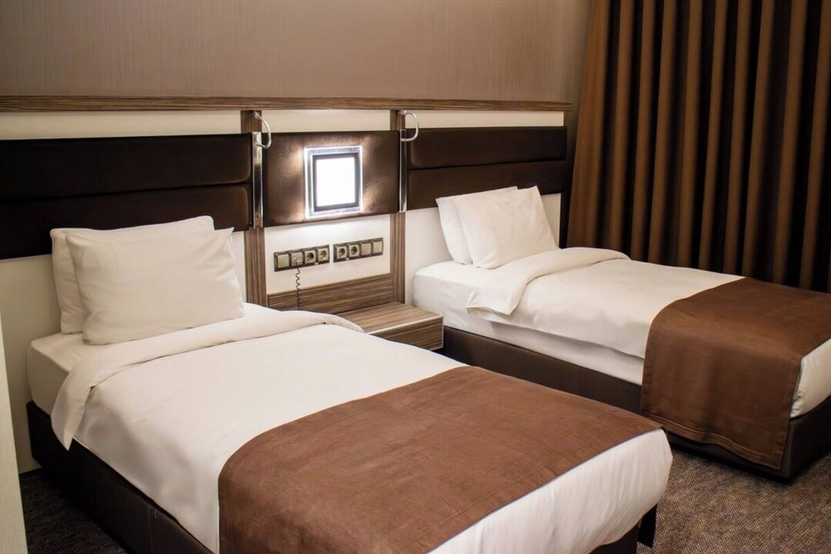 A hotel room with two single beds, a bedside table, a lamp, and a window with curtains.