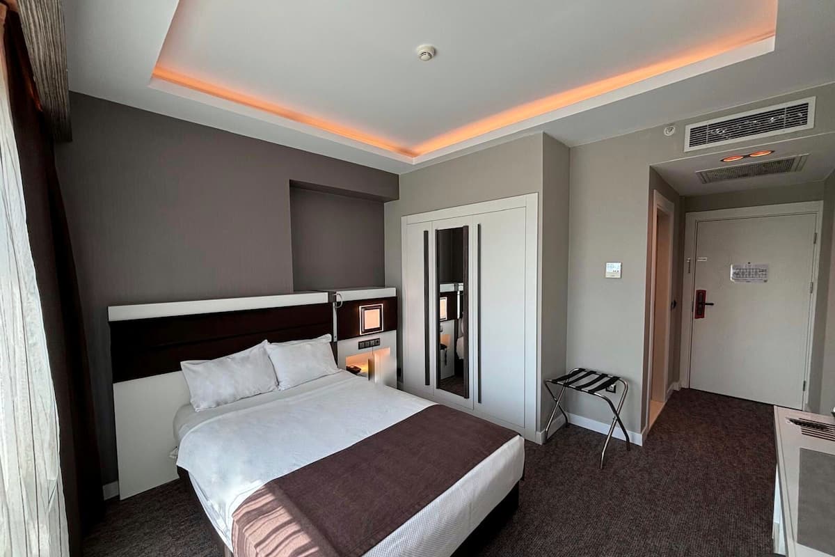 A hotel room with a large bed, a desk, a chair, a wardrobe, and a door.
