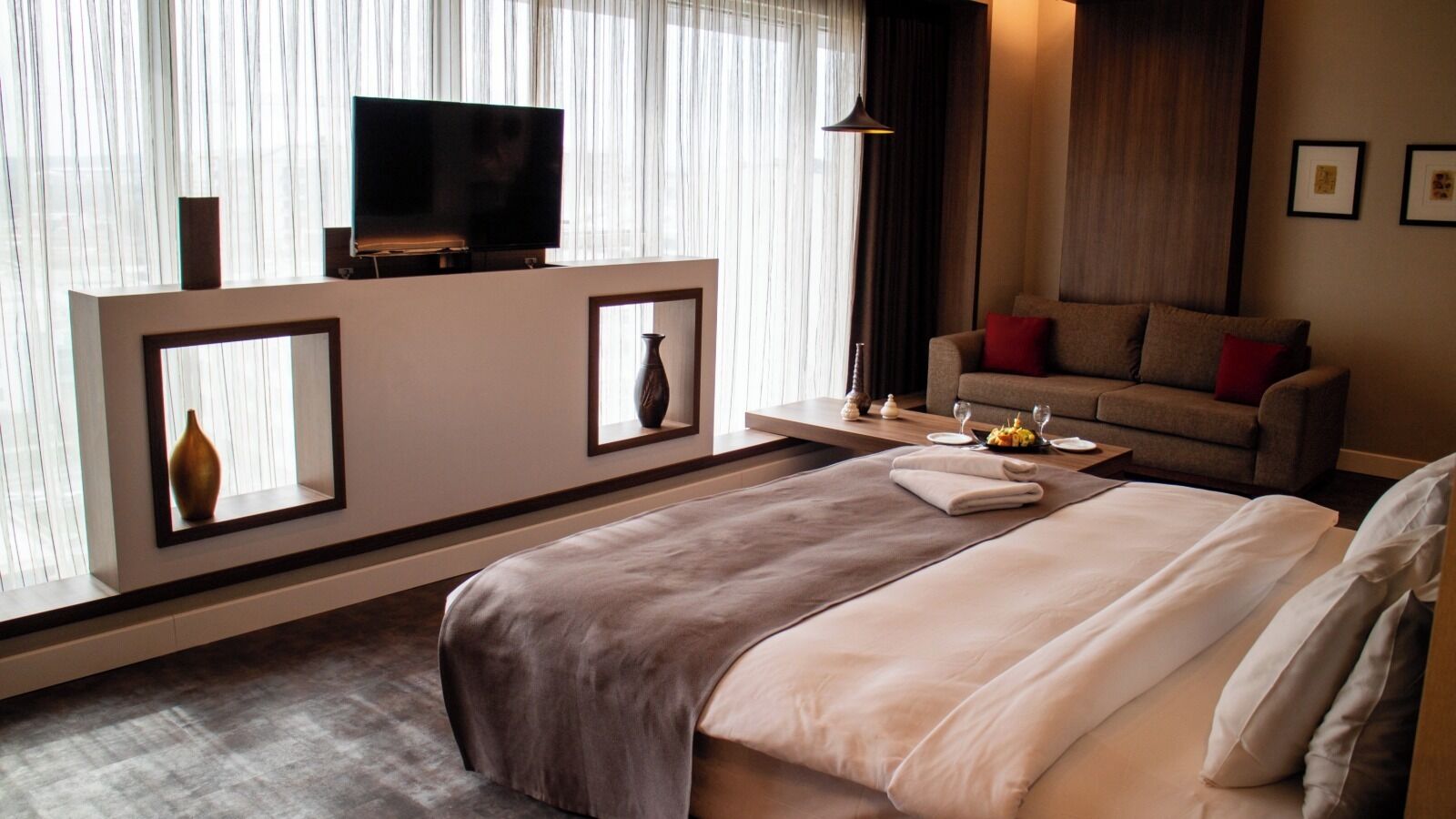 Ein Hotelzimmer mit Bett, Fernseher auf einem Schrank, einer Couch und einem Esstisch mit Gläsern und einem Teller Essen.