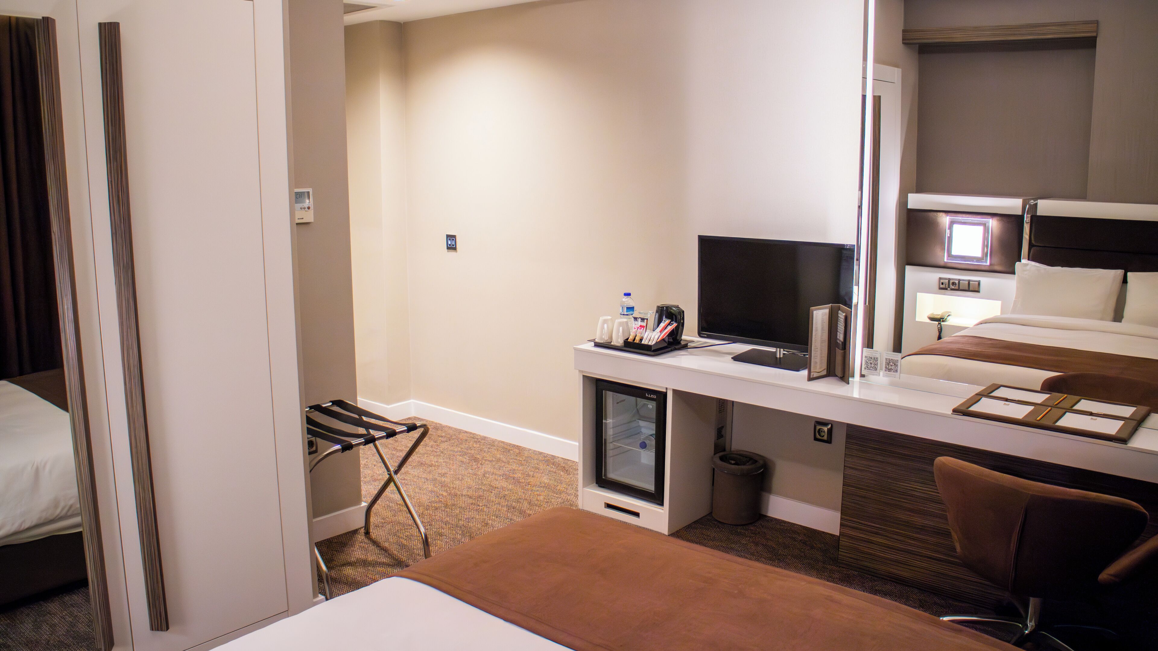 A hotel room with a bed, a desk with a computer, a chair, and a small TV.