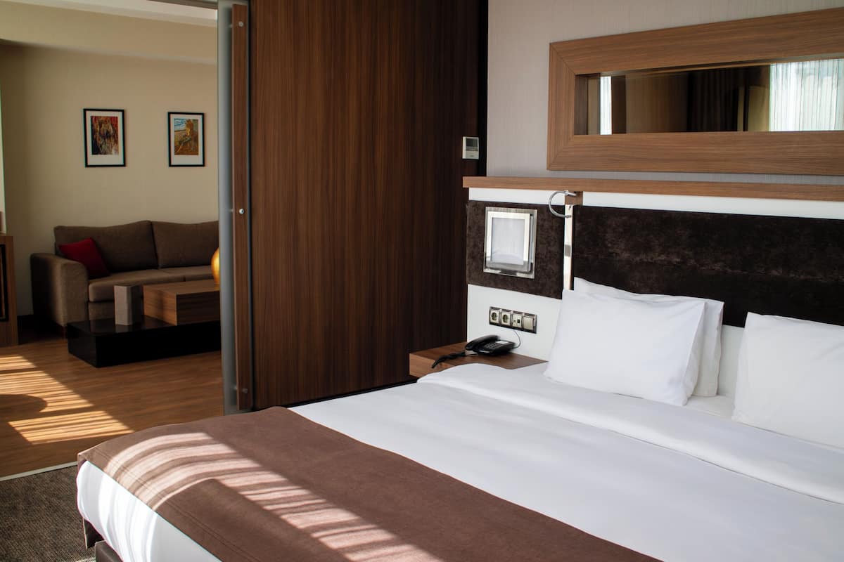 A hotel room with a large bed, a bedside telephone, a wooden headboard, and a small desk with a lamp.