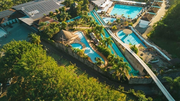 An aerial view of a resort with multiple swimming pools, a bridge, and lush greenery. - Villa Di Acqua Hotel (Gaspar)