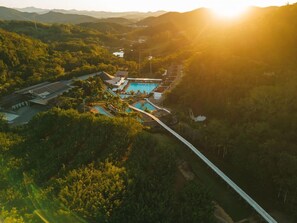 Luftaufnahme eines Resorts mit Schwimmbad, Brücke und dichter Bepflanzung.