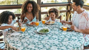 A family dining at a table with a floral tablecloth, surrounded by large windows with a view of palm trees. - Villa Di Acqua Hotel (Gaspar)