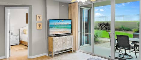 A spacious living room with a television displaying 'Legacy Vacations' and a view of the ocean through large sliding glass doors.