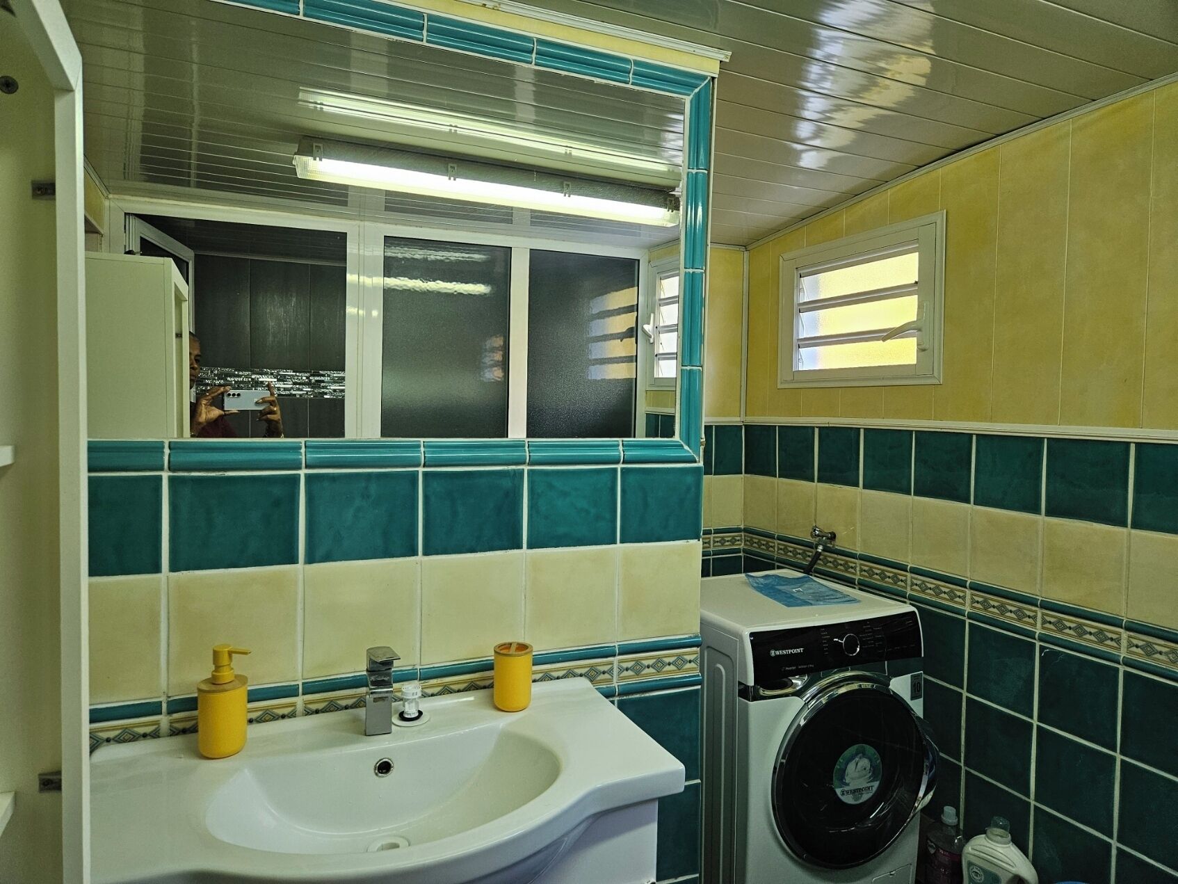 Casa de banho com lavatório, espelho e máquina de lavar roupa.