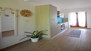Cocina moderna con armarios de madera, horno empotrado y un fregadero. Hay una planta en maceta en el suelo y un adorno colgando en la pared.