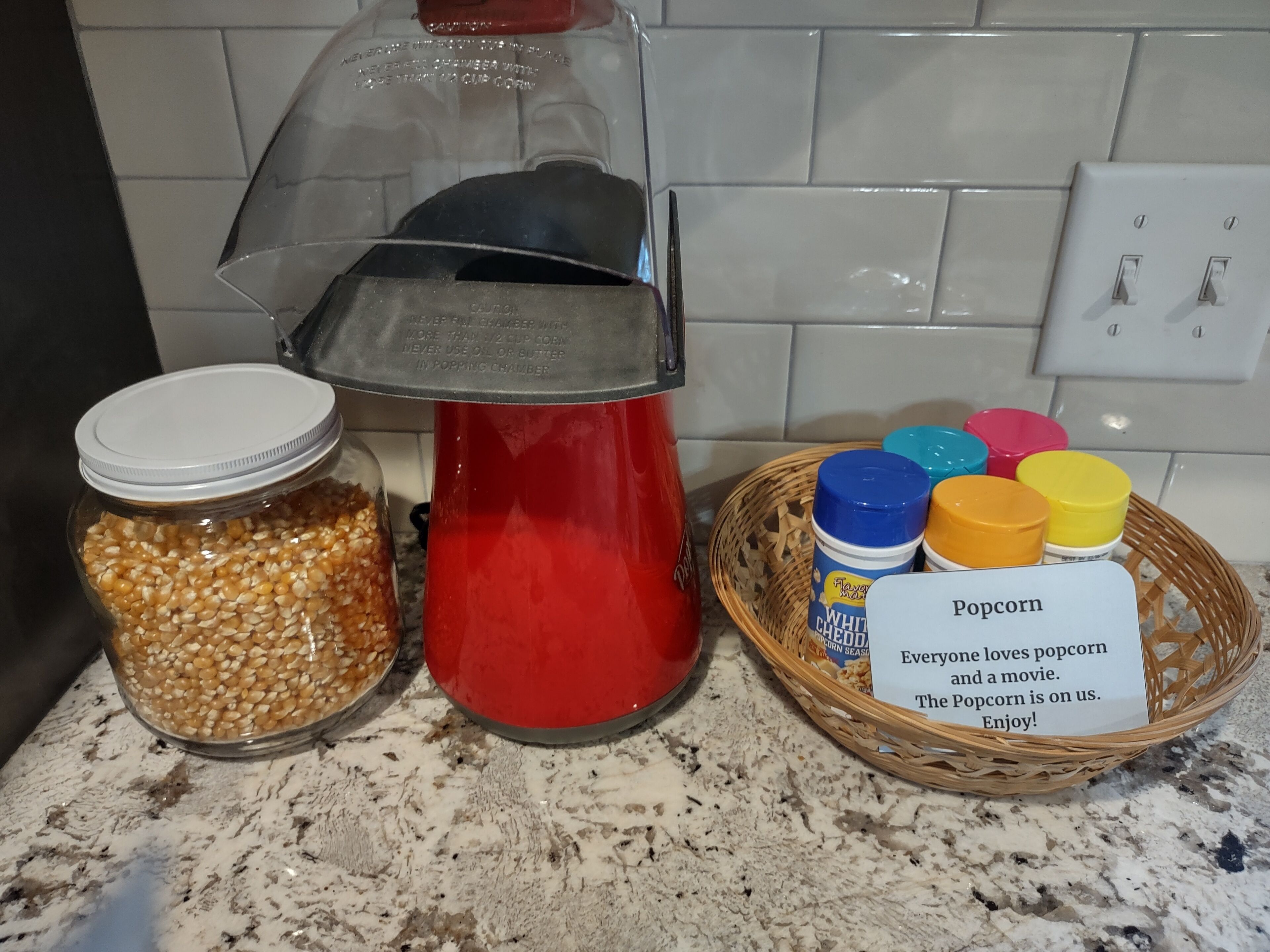 Une machine à pop-corn, un bocal de grains de maïs à éclater et un panier contenant des récipients à pop-corn ainsi qu’une pancarte.