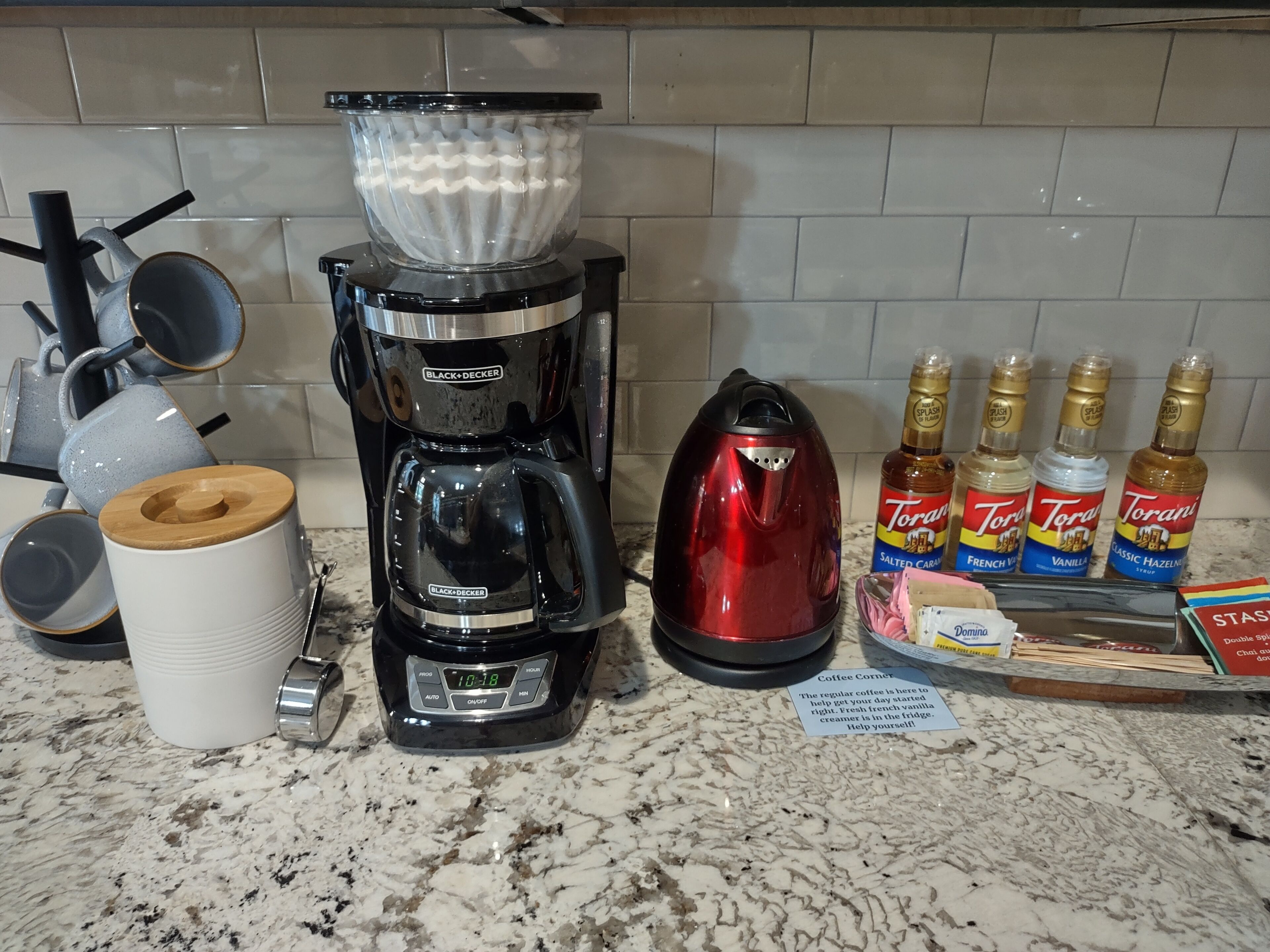 A kitchen counter with a coffee maker, a kettle, and Torani syrup bottles.