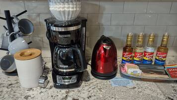 A kitchen counter with a coffee maker, a kettle, and Torani syrup bottles.