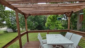 A wooden deck with a table and chairs, surrounded by a wooden railing and trees.