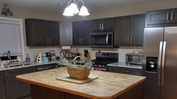 A modern kitchen with dark cabinets, a central island, stainless steel appliances, and a hanging light fixture.