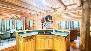 A wooden cabin interior with a kitchen area featuring a large island, wooden cabinets, and a stone wall. - Spacious Cabin for 14 on Fightingtown Creek – Private Trout Fishing Retreat (McCaysville)
