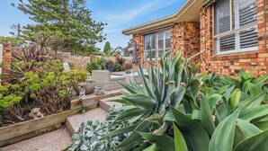 Une maison avec une façade en briques, un patio doté de mobilier d’extérieur et agrémenté de diverses plantes.
