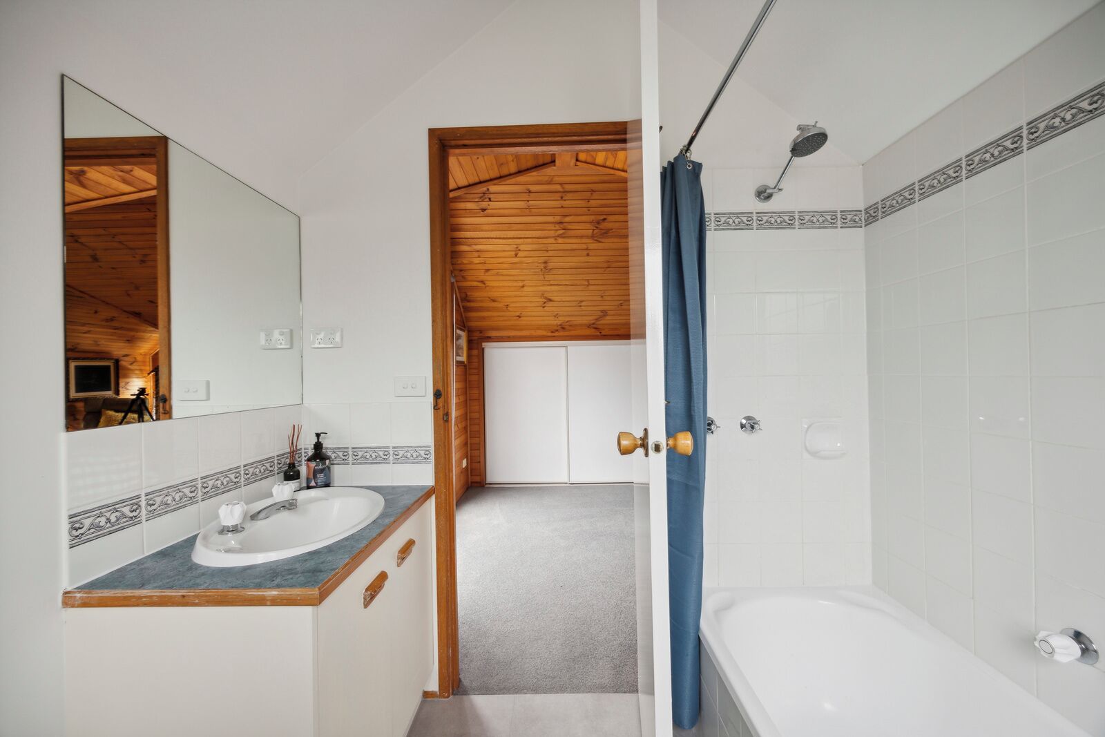 Ein Badezimmer mit Holzbalkendecke, einem Waschbecken mit Spiegel, einer Duschkabine mit Vorhang und gefliesten Wänden.