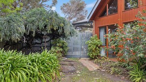Un jardin avec une clôture en bois, diverses plantes et un bâtiment doté de grandes fenêtres.