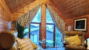 L’intérieur d’un chalet accueillant, avec un canapé en cuir, un fauteuil et une grande fenêtre agrémentée de rideaux.