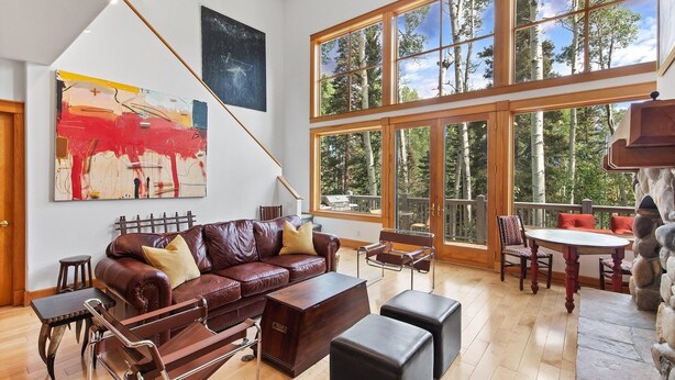 A spacious living room with a large window, a leather sofa, a wooden coffee table, and a stone fireplace. - Polecat Chalet 4 Bedroom Home by RedAwning (Telluride)