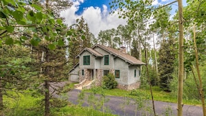 A two-story stone house with a stone foundation and green shutters, surrounded by dense forest and a clear sky. - Polecat Chalet 4 Bedroom Home by RedAwning (Telluride)