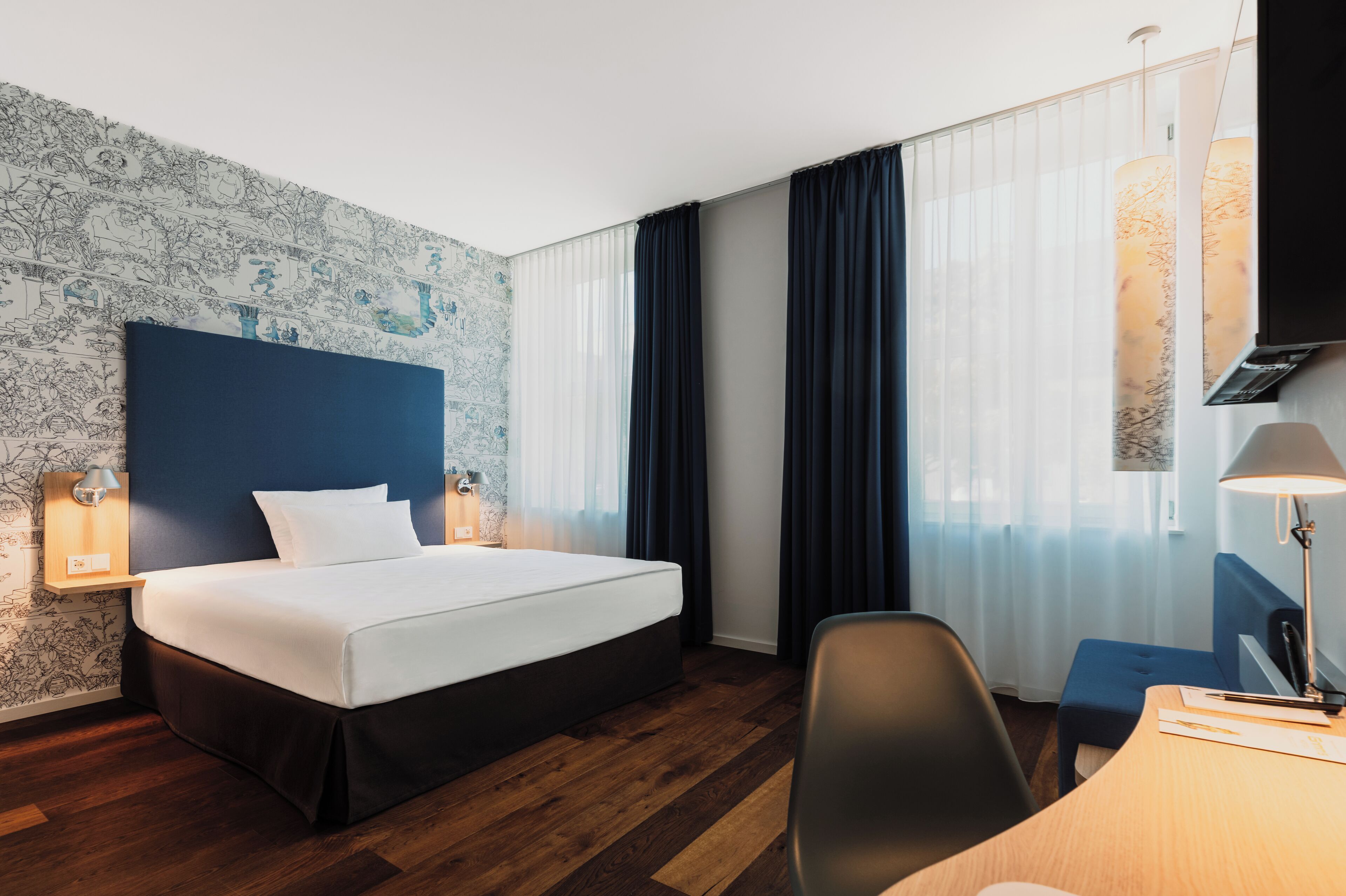 Una habitación de hotel con una cama grande, un escritorio con silla, una lámpara y un televisor.