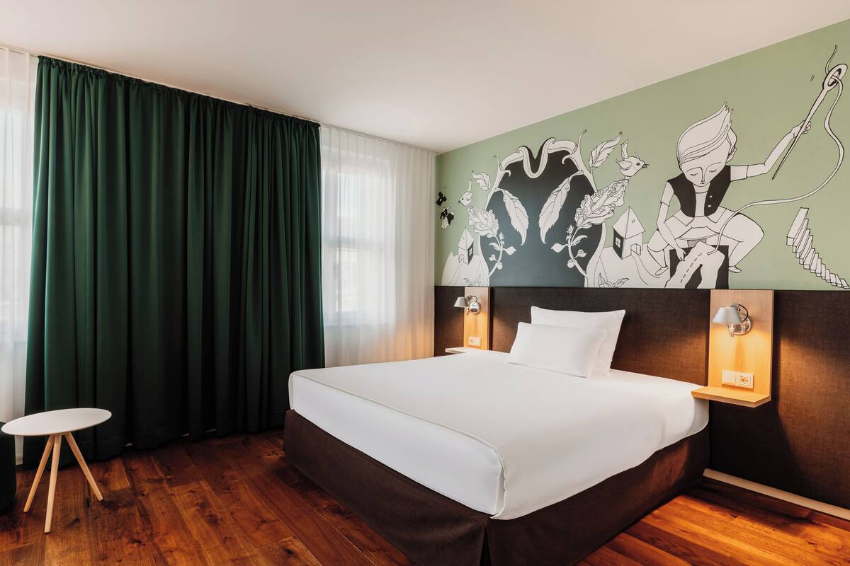Une chambre d’hôtel avec un grand lit, une petite table, une chaise et une fresque murale.