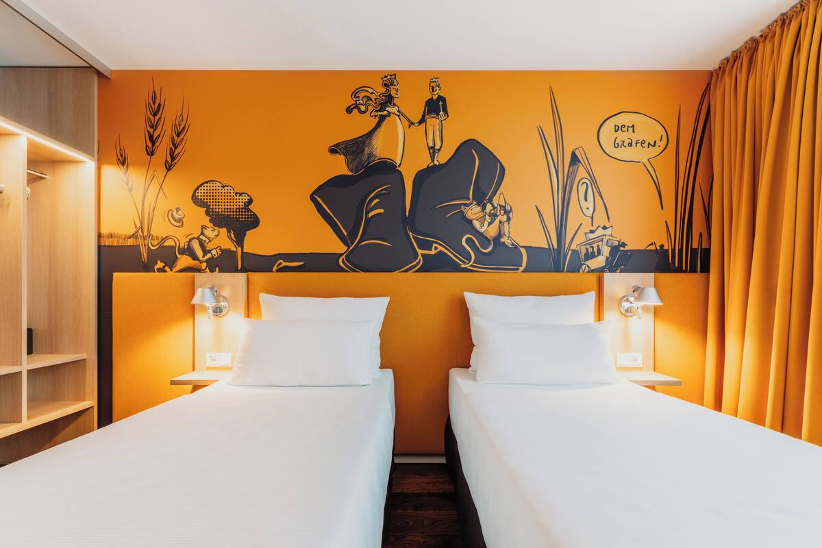 Une chambre d’hôtel avec deux lits, une fresque murale et une étagère en bois.
