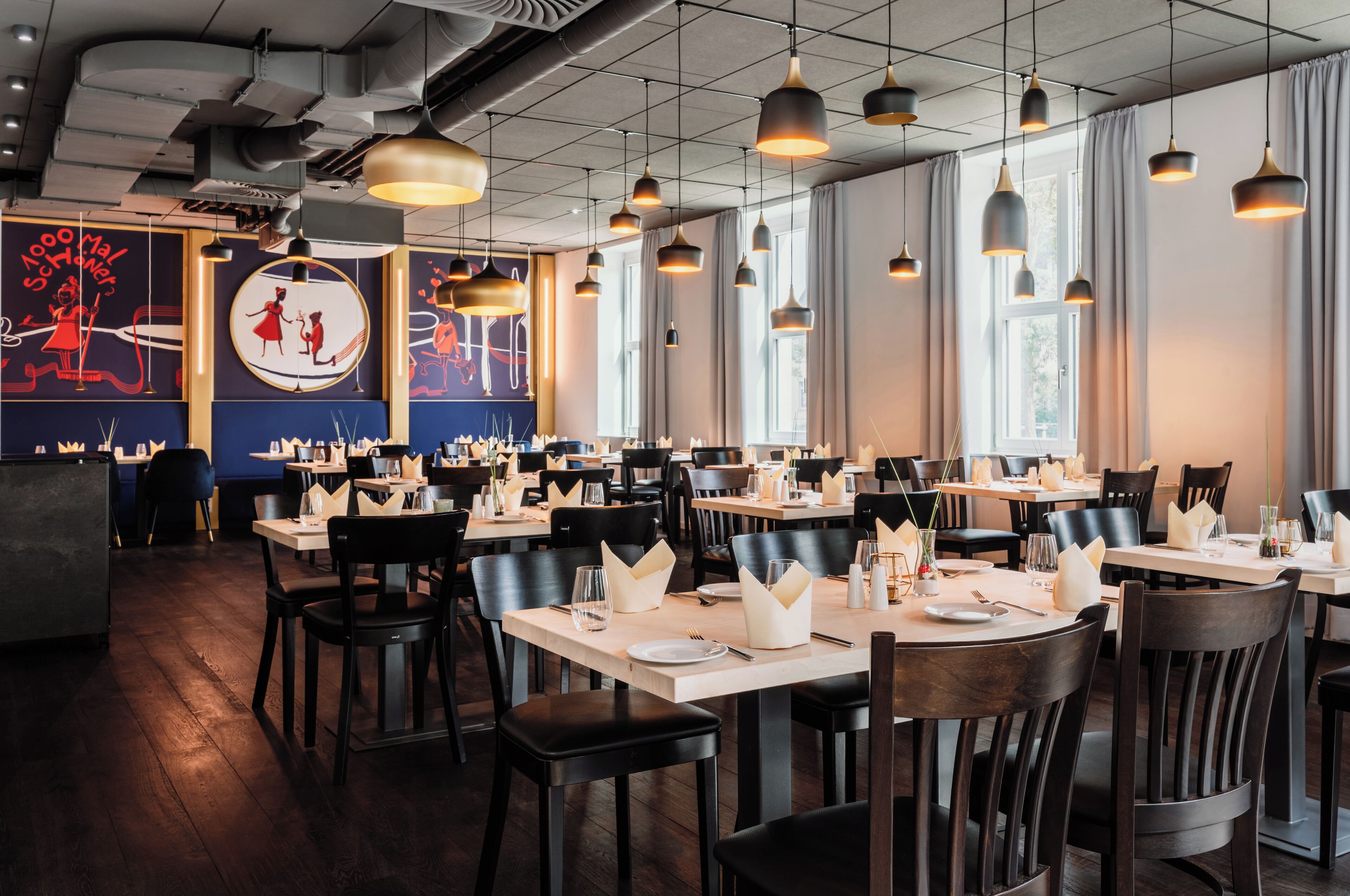 A restaurant with multiple tables, black chairs, and pendant lighting.