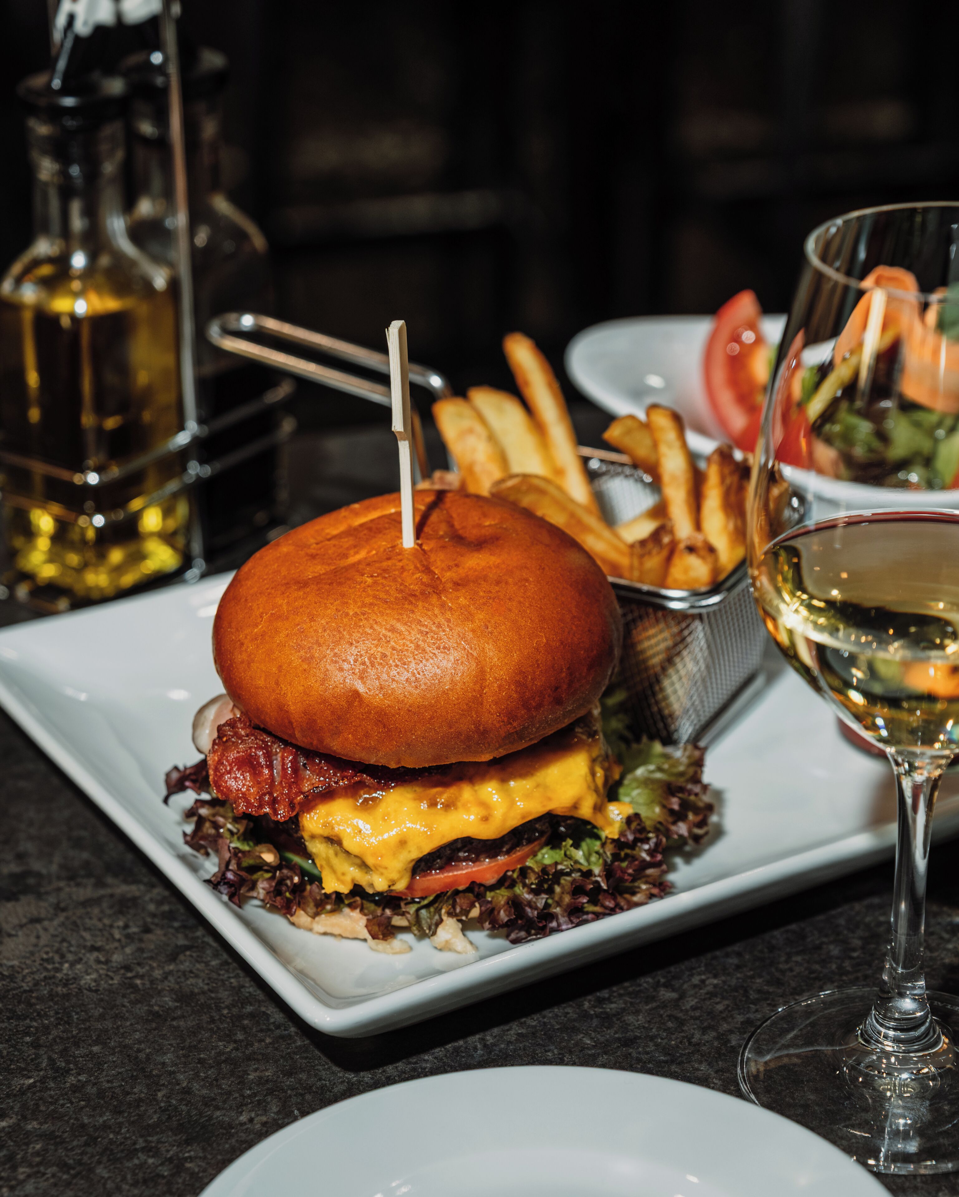 Un hamburger accompagné de frites et d’un verre de vin, le tout servi sur une assiette.