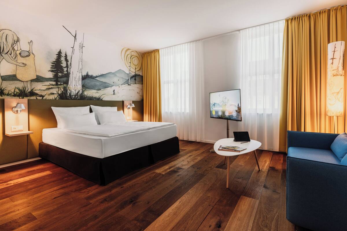 Une chambre d’hôtel moderne avec un grand lit, une petite table, une télévision et un canapé.