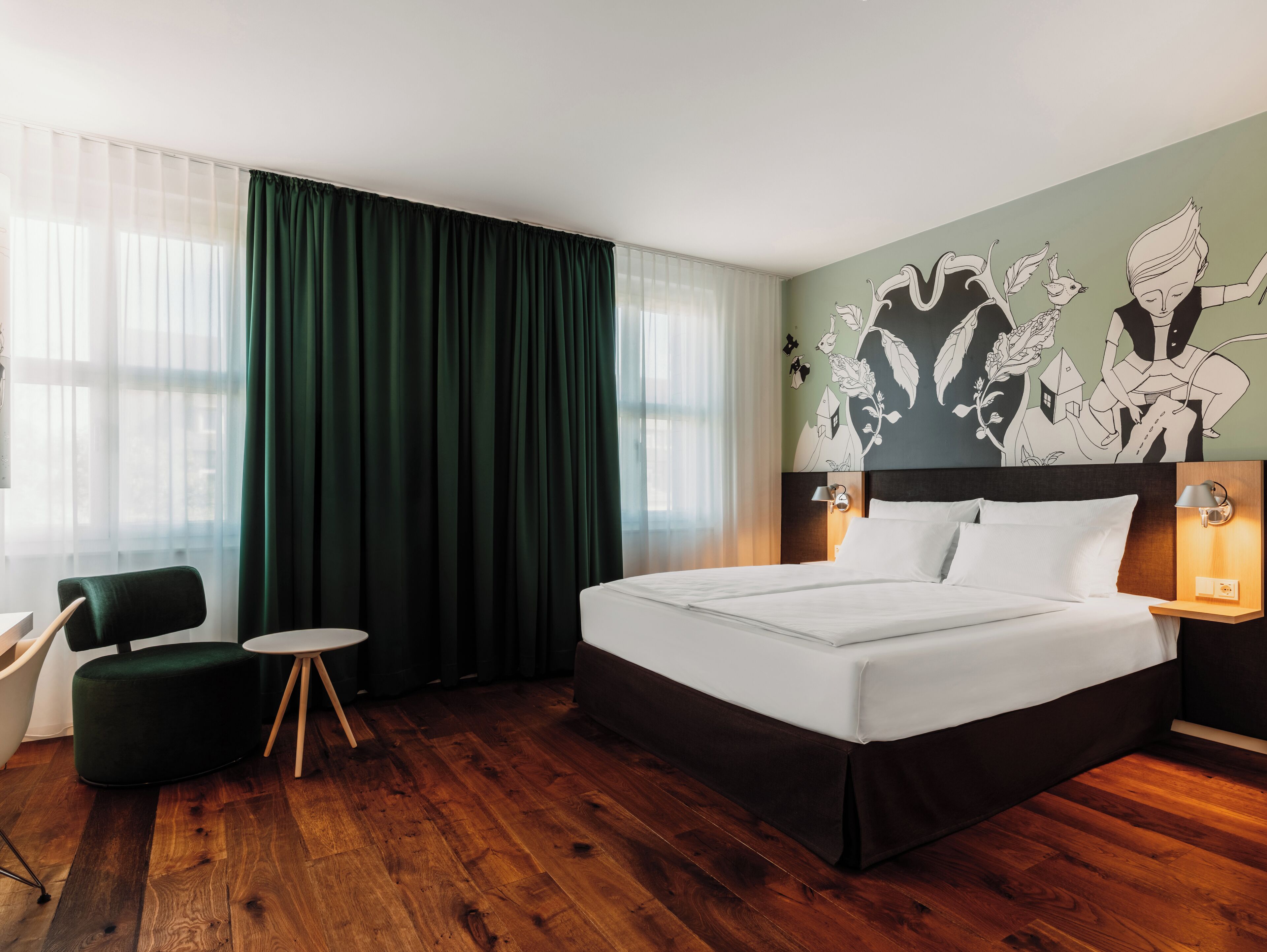 A hotel room with a large bed, a small round table, a chair, and a wall mural.