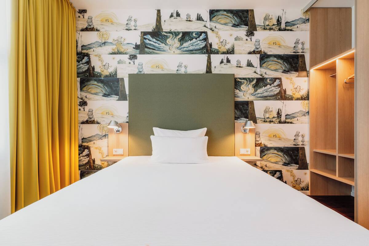 Une chambre d’hôtel avec un lit, une tête de lit, des œuvres d’art murales et une armoire en bois.