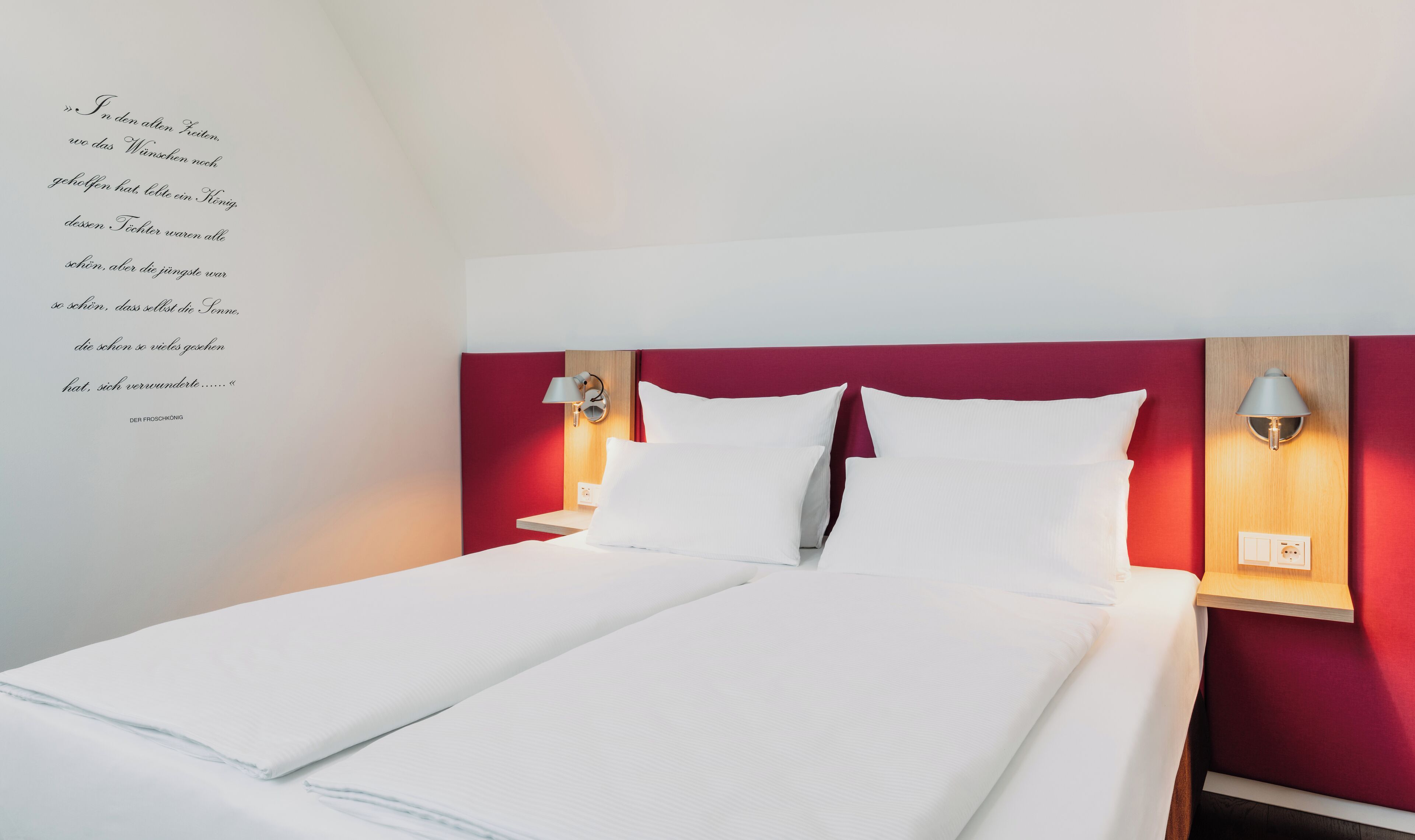 Una cama doble con ropa blanca de cama, un cabecero rojo y dos lámparas de noche.
