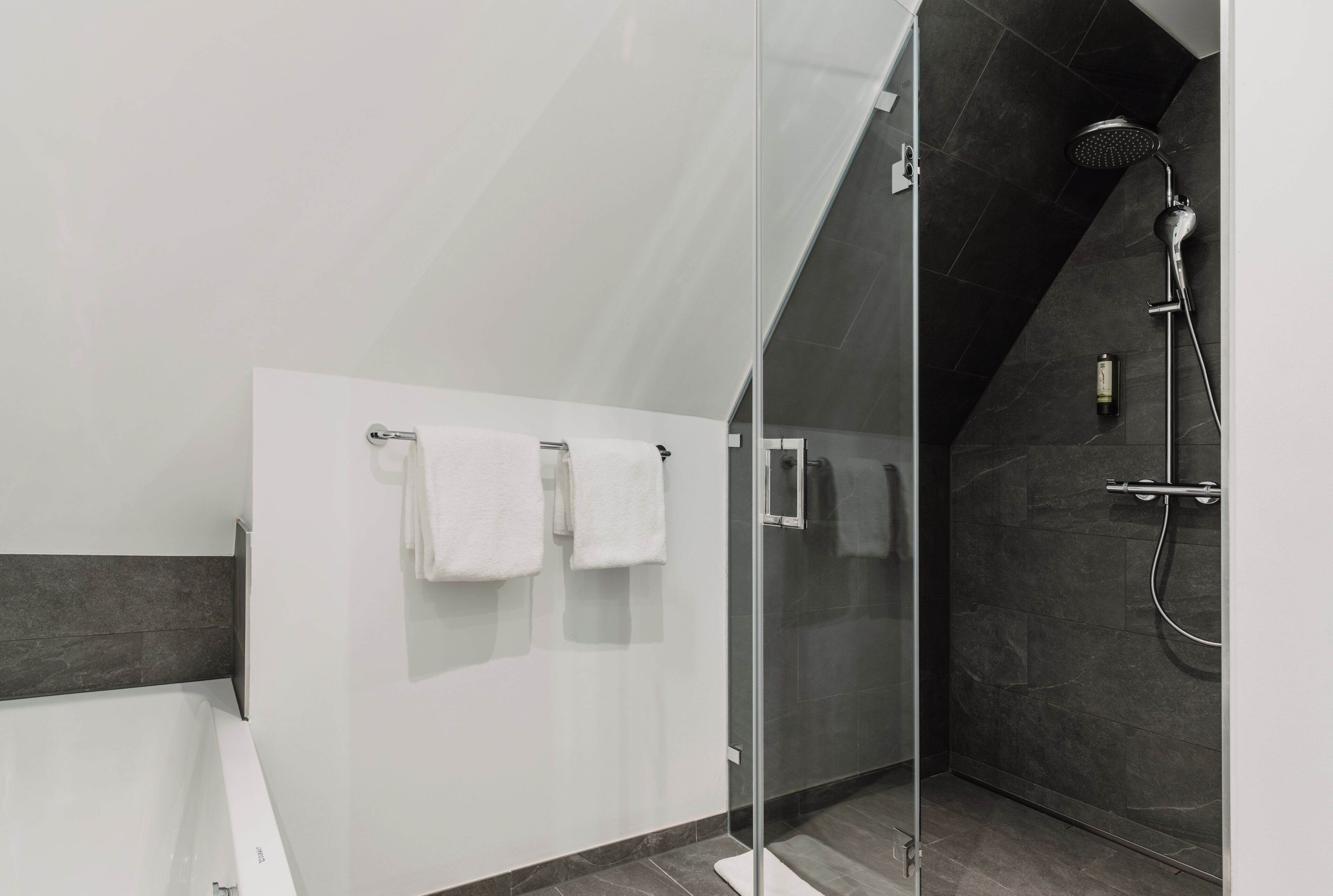 Une salle de bain moderne avec une douche à parois de verre, une baignoire et deux serviettes blanches accrochées au mur.
