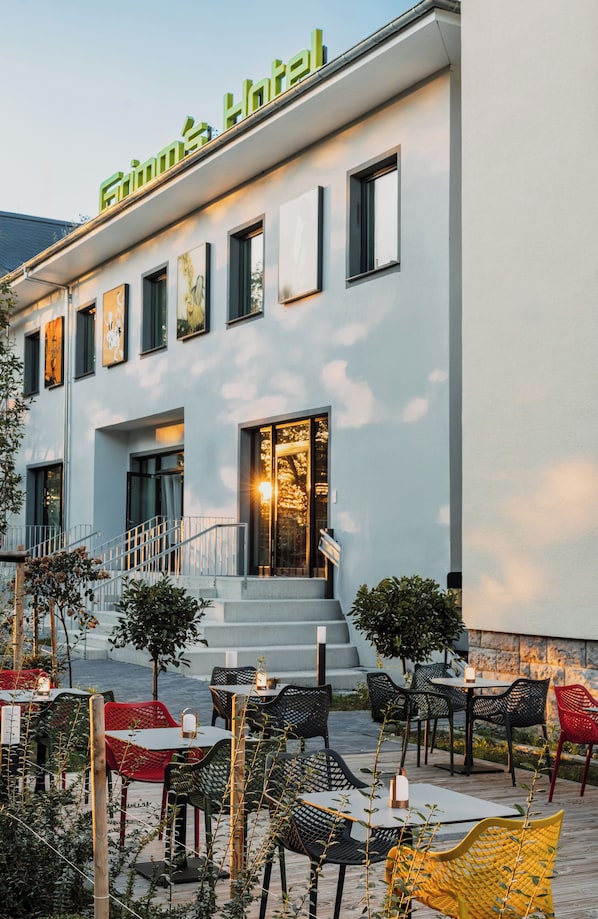 Exterior de un hotel con mesas al aire libre, una escalera y un cartel que dice "Fiume Hotel".