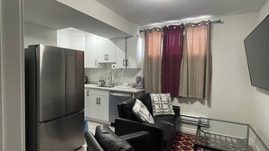 Un espacio habitable compacto con kitchenette, un sofá, una mesa de centro y un televisor montado en la pared.