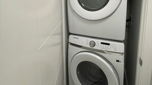 Un lavadero pequeño y de dos puertas con un diseño moderno, que incluye una lavadora y secadora Samsung apiladas verticalmente.