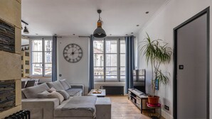 A modern living room with a sofa, a coffee table, a TV, and a large window with curtains. - Spacious appartment in the heart of Angers - 6 PAX (Angers)
