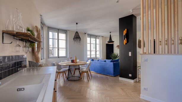 A modern kitchen with a central island, a dining area with a round table, and a blue sofa in the living area. - Spacious appartment in the heart of Angers - 6 PAX (Angers)