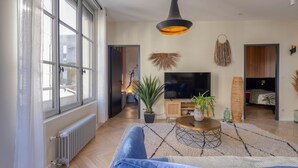 A modern living room with a large window, a sofa, a TV, and a radiator. - Spacious appartment in the heart of Angers - 6 PAX (Angers)